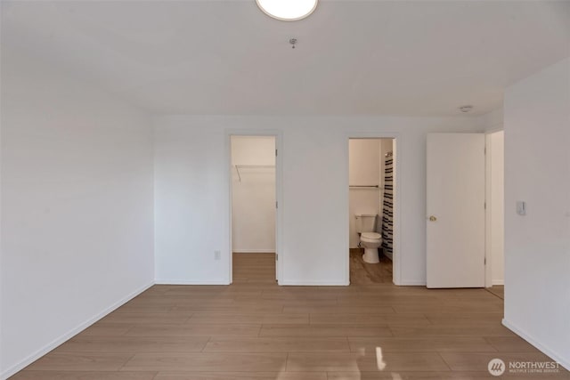12050 15th Ave NE Unit 404, Seattle, WA 98125 - unfurnished bedroom featuring light wood-type flooring, a spacious closet, baseboards, connected bathroom, and a closet