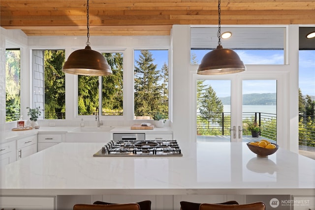 kitchen featuring stainless steel gas cooktop, a sink, white cabinetry, a water view, and pendant lighting