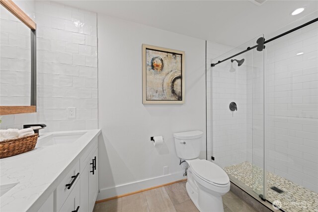 bathroom with toilet, a shower stall, baseboards, wood finished floors, and double vanity