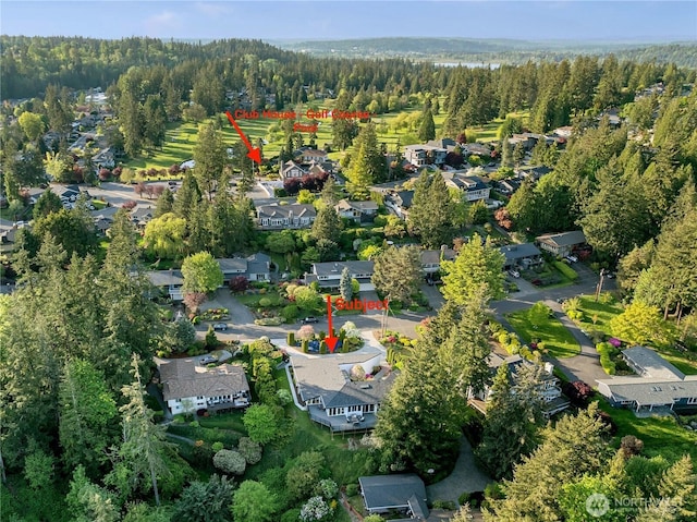 aerial view of property and surrounding area featuring a forest and nearby suburban area