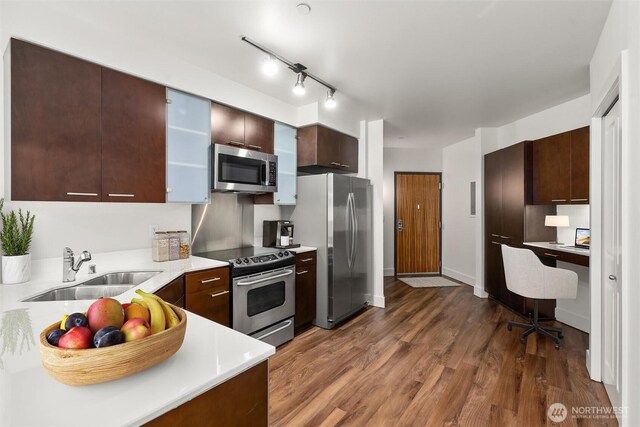 kitchen with appliances with stainless steel finishes, a sink, dark wood-style floors, light countertops, and dark brown cabinets