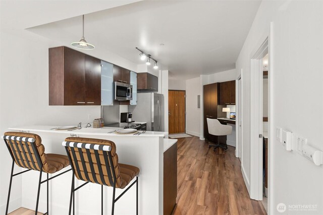 kitchen with appliances with stainless steel finishes, a peninsula, a kitchen breakfast bar, light countertops, and wood finished floors