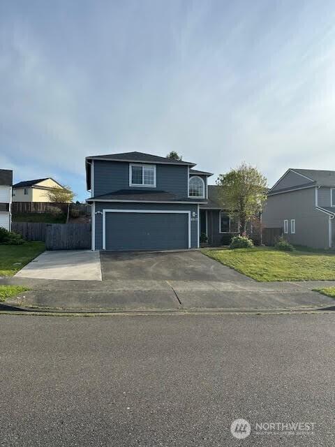 traditional-style home featuring an attached garage, concrete driveway, fence, and a front lawn