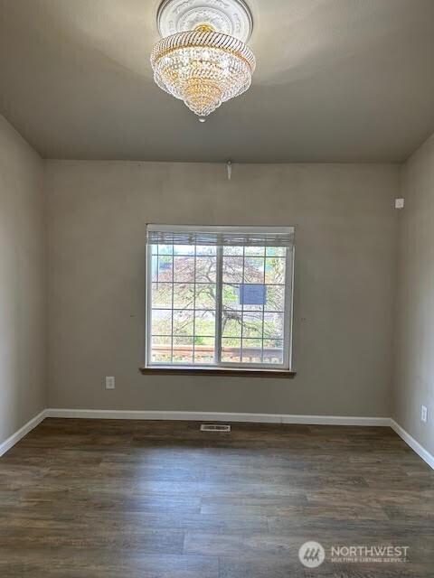 unfurnished room with an inviting chandelier, dark wood-type flooring, and baseboards