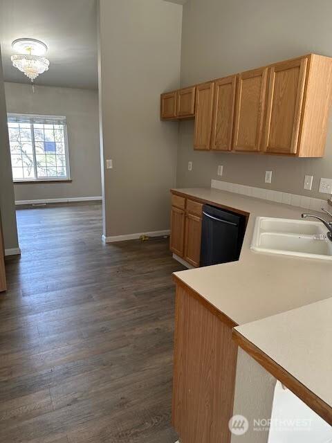 kitchen featuring a sink, black dishwasher, dark wood-style flooring, light countertops, and baseboards
