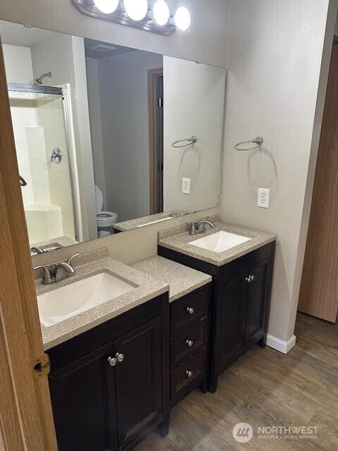 bathroom featuring wood finished floors, a stall shower, two vanities, and a sink