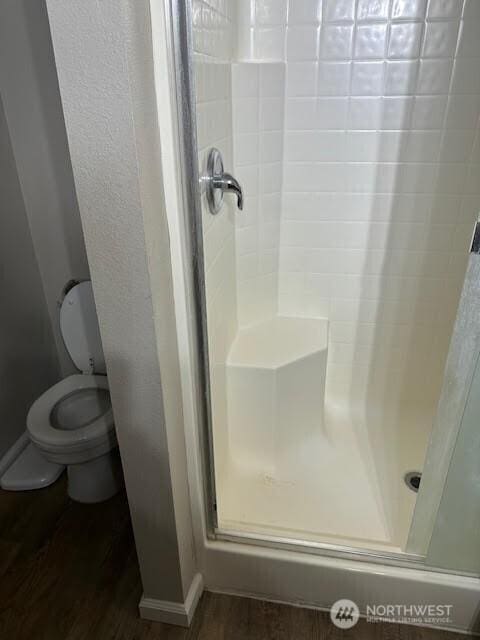 full bath with toilet, baseboards, wood finished floors, and a shower stall