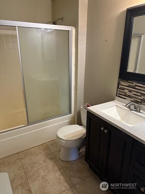 bathroom featuring vanity, combined bath / shower with glass door, toilet, and tile patterned flooring