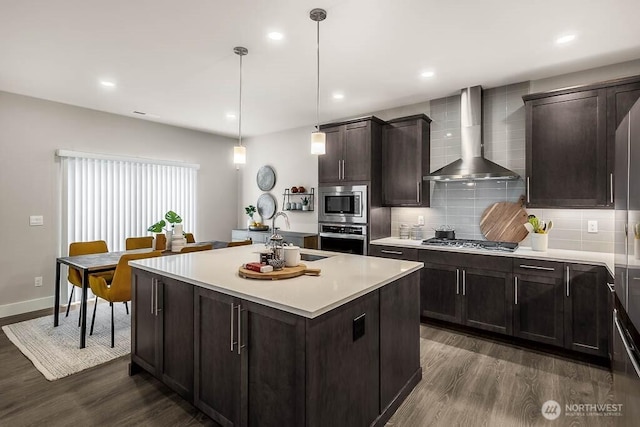 kitchen featuring wall chimney range hood, appliances with stainless steel finishes, a sink, and dark wood-type flooring