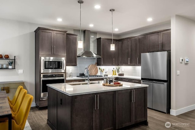 kitchen with wall chimney range hood, stainless steel appliances, dark brown cabinets, and dark wood-style floors