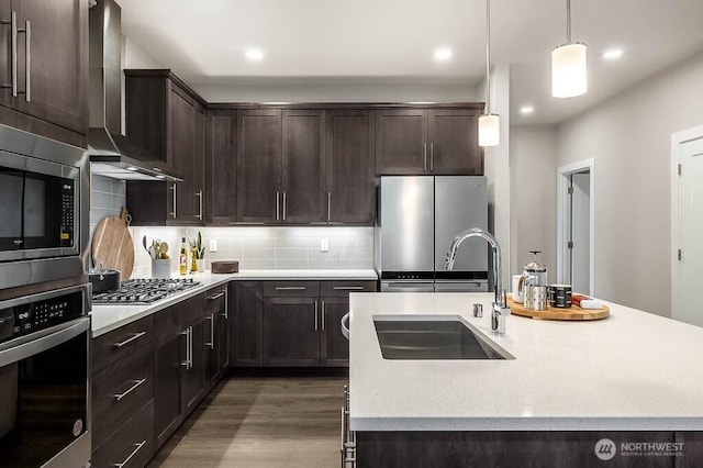 kitchen featuring wood finished floors, a sink, wall chimney exhaust hood, stainless steel appliances, and dark brown cabinetry