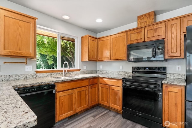 kitchen with a sink, black appliances, recessed lighting, light stone countertops, and light wood-style floors