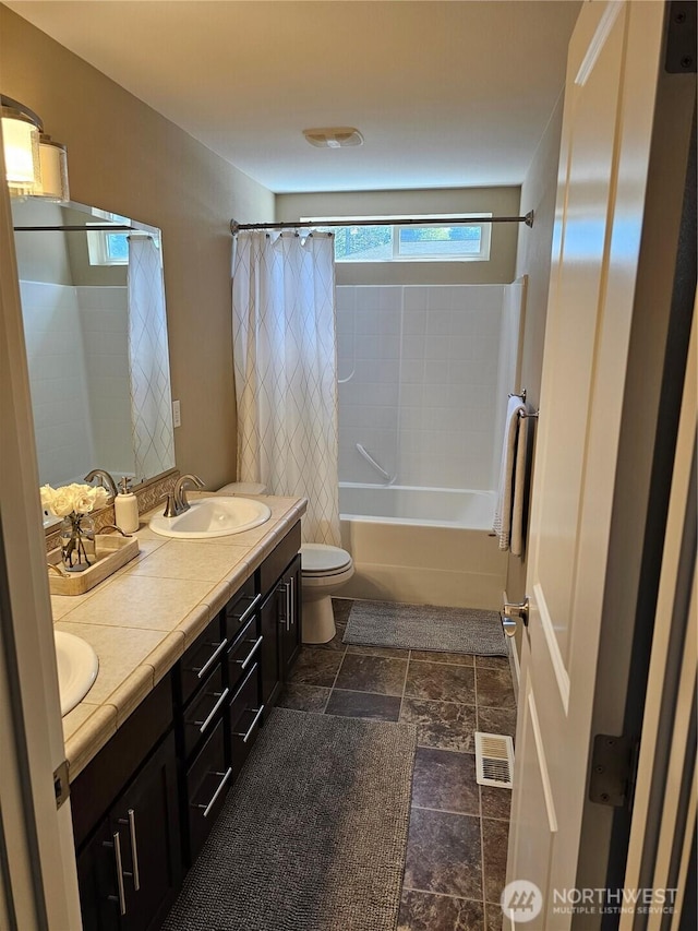 full bath with double vanity, toilet, shower / bath combination with curtain, stone finish flooring, and a sink