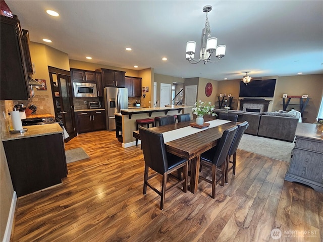 dining area featuring a fireplace, ceiling fan with notable chandelier, dark wood-style floors, and recessed lighting