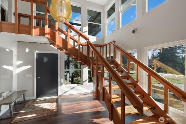 stairway with a towering ceiling, baseboards, and wood finished floors