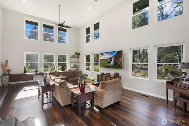 living area with baseboards, dark wood finished floors, ceiling fan, visible vents, and a towering ceiling