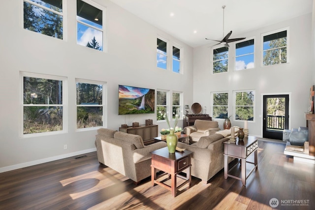 living room with a towering ceiling, visible vents, ceiling fan, dark wood-style floors, and baseboards