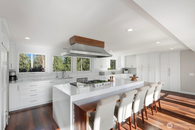 kitchen with a kitchen bar, a sink, white cabinets, dark wood finished floors, and light countertops