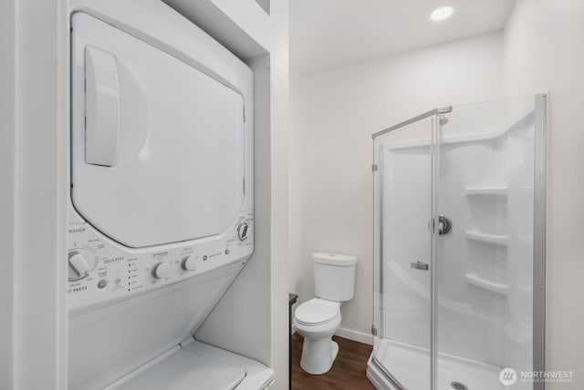 full bath with stacked washing maching and dryer, toilet, a shower stall, and wood finished floors