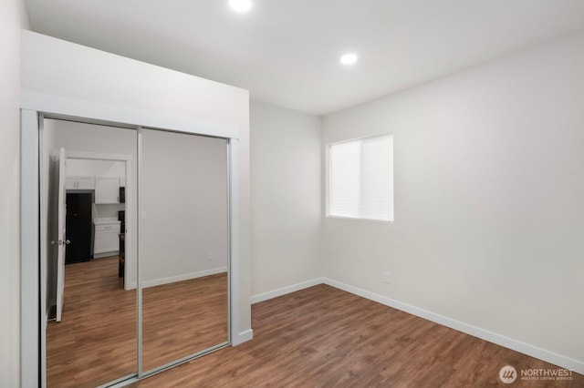 unfurnished bedroom with a closet, wood finished floors, freestanding refrigerator, recessed lighting, and baseboards