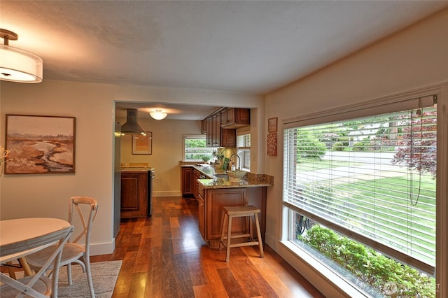 10733 14th Ave NE, Seattle, WA 98125 - kitchen featuring wall chimney range hood, brown cabinetry, dark wood-style flooring, baseboards, and stone counters