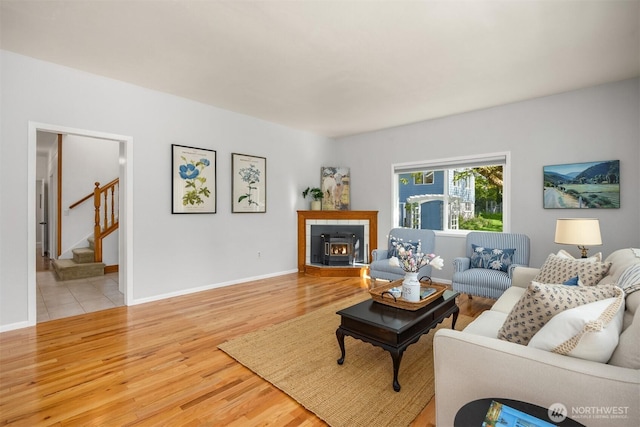 living area with stairs, baseboards, light wood-style flooring, and a tile fireplace