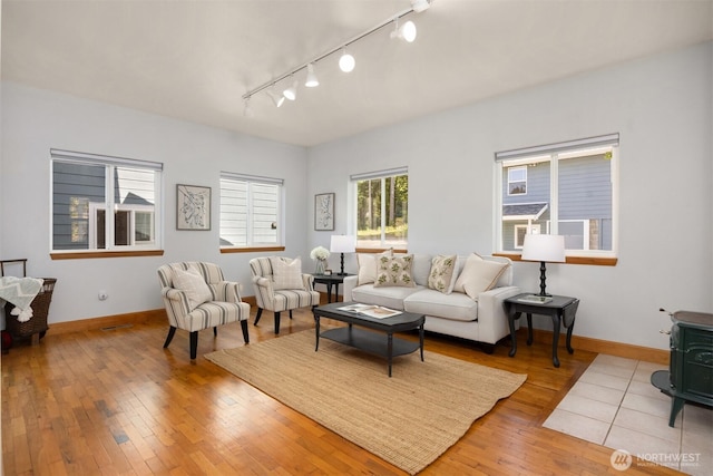 living room featuring track lighting, a wood stove, baseboards, and hardwood / wood-style flooring