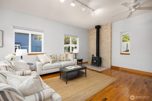 living area with a wood stove, rail lighting, ceiling fan, and hardwood / wood-style flooring