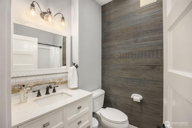 bathroom featuring a shower with curtain, toilet, wooden walls, vanity, and backsplash