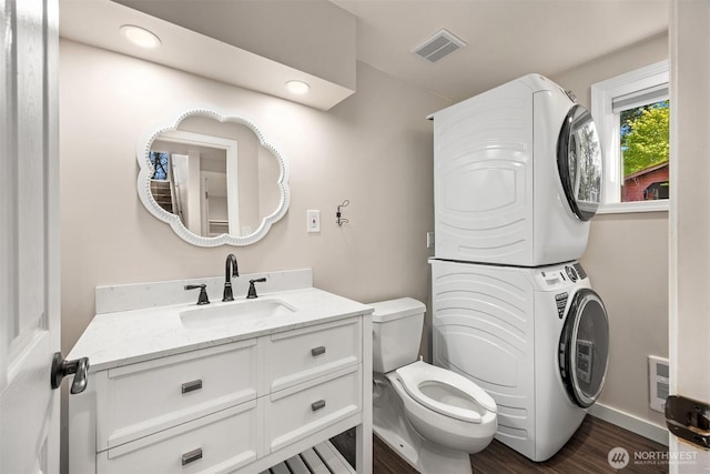 bathroom featuring toilet, wood finished floors, stacked washer / dryer, vanity, and visible vents