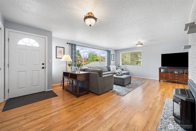 living room with light wood-type flooring, a textured ceiling, a wood stove, and baseboards