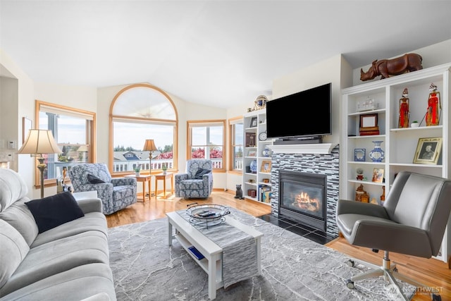 living room with plenty of natural light, a tiled fireplace, wood finished floors, and lofted ceiling