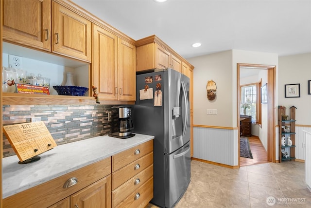 kitchen with stainless steel fridge, tasteful backsplash, wainscoting, light stone counters, and recessed lighting