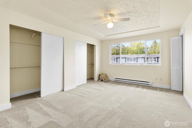 unfurnished bedroom featuring a baseboard heating unit, multiple closets, a textured ceiling, carpet flooring, and baseboards