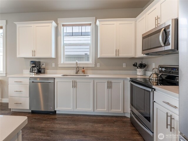 kitchen featuring stainless steel appliances, a sink, dark wood finished floors, white cabinetry, and light countertops