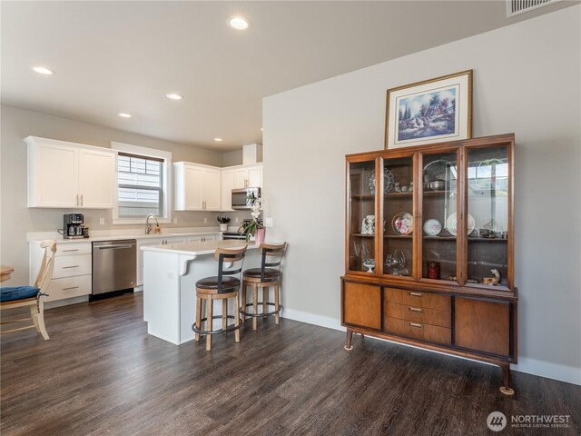 kitchen with appliances with stainless steel finishes, a breakfast bar area, light countertops, white cabinetry, and dark wood finished floors