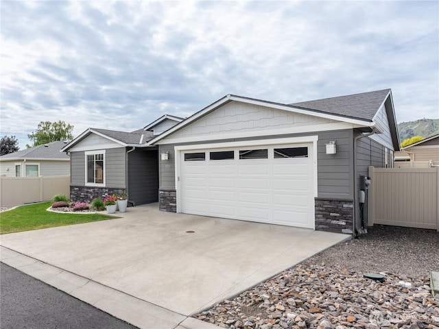 view of front of home with stone siding, a garage, fence, concrete driveway, and roof with shingles