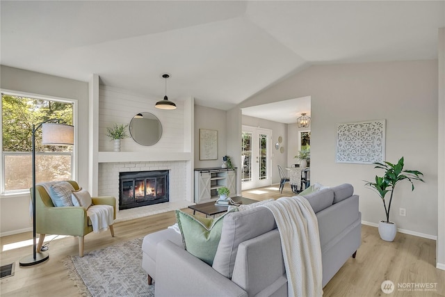 living area with a fireplace, lofted ceiling, baseboards, and light wood-type flooring