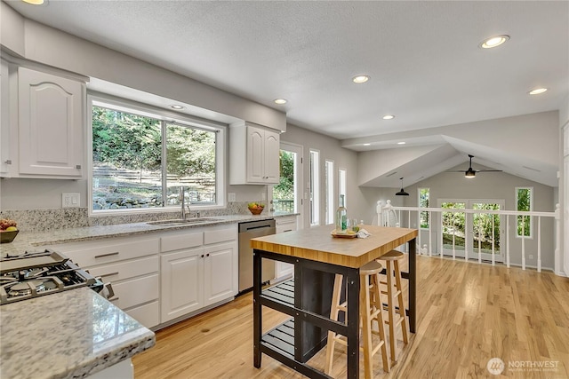kitchen with light wood-style floors, a sink, stainless steel dishwasher, and white cabinets