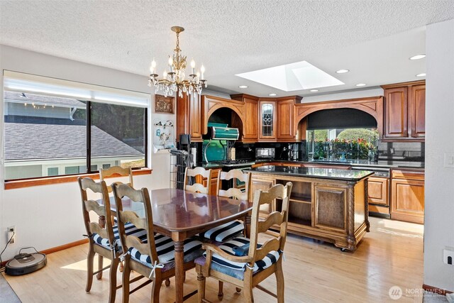 dining area featuring a skylight, light wood-style flooring, a chandelier, a textured ceiling, and recessed lighting