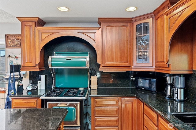 kitchen featuring stainless steel gas range, black microwave, decorative backsplash, glass insert cabinets, and brown cabinets