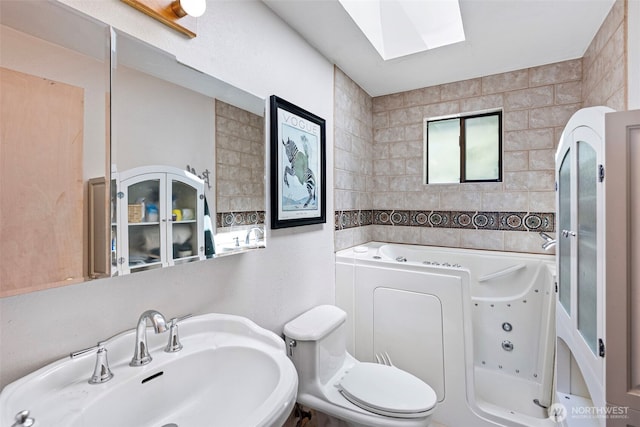 full bath featuring a sink, a skylight, a jetted tub, toilet, and tile walls