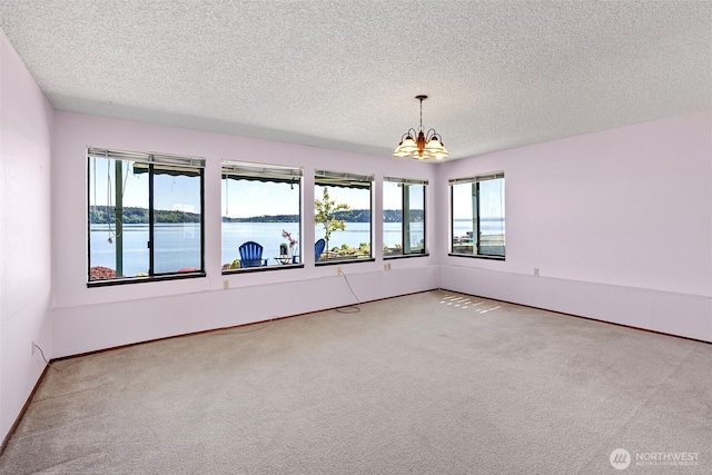 unfurnished room featuring a chandelier, plenty of natural light, carpet flooring, a textured ceiling, and a water view