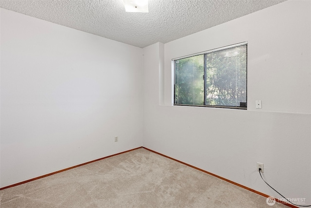 carpeted spare room featuring a textured ceiling and baseboards