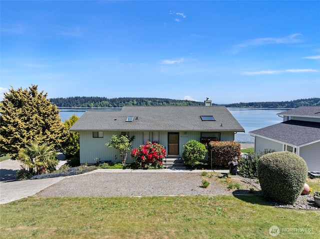 ranch-style home featuring a chimney, a water view, a front lawn, and roof with shingles