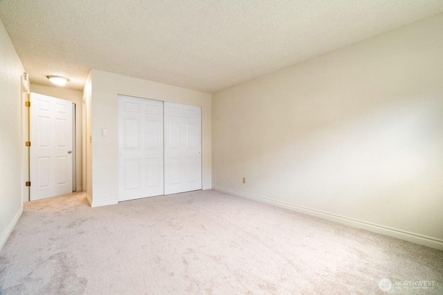 unfurnished bedroom with light colored carpet, a textured ceiling, baseboards, and a closet