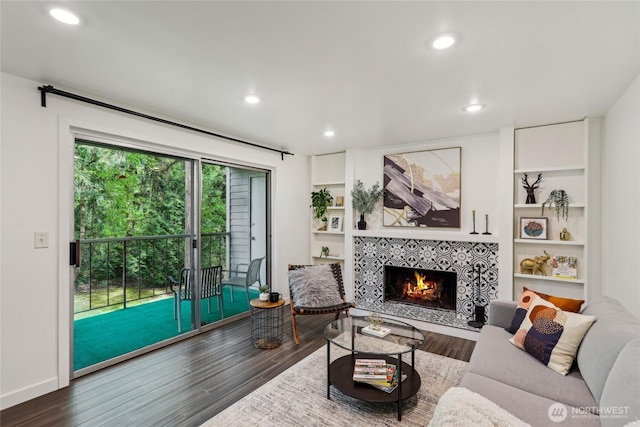 living area featuring a tiled fireplace, wood finished floors, recessed lighting, and built in shelves