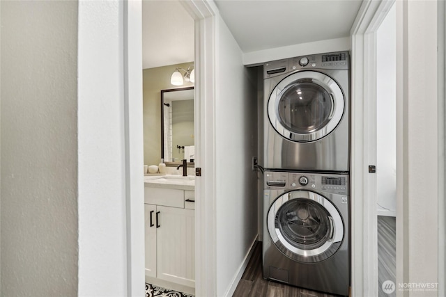 clothes washing area with stacked washer / dryer, wood finished floors, and baseboards