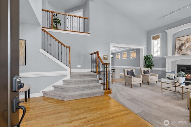 foyer with stairs, wood finished floors, a high end fireplace, high vaulted ceiling, and track lighting
