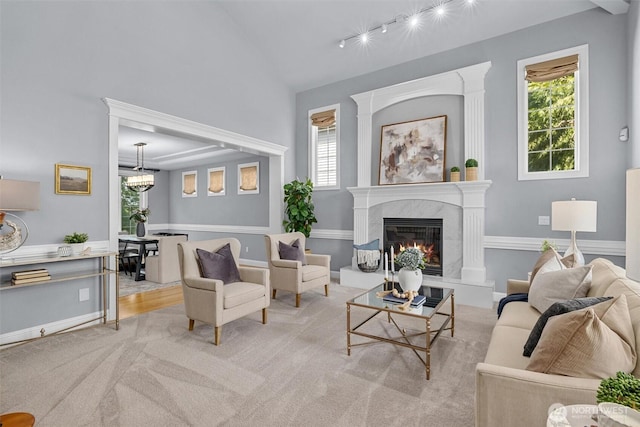 living area with plenty of natural light, lofted ceiling, track lighting, a high end fireplace, and carpet